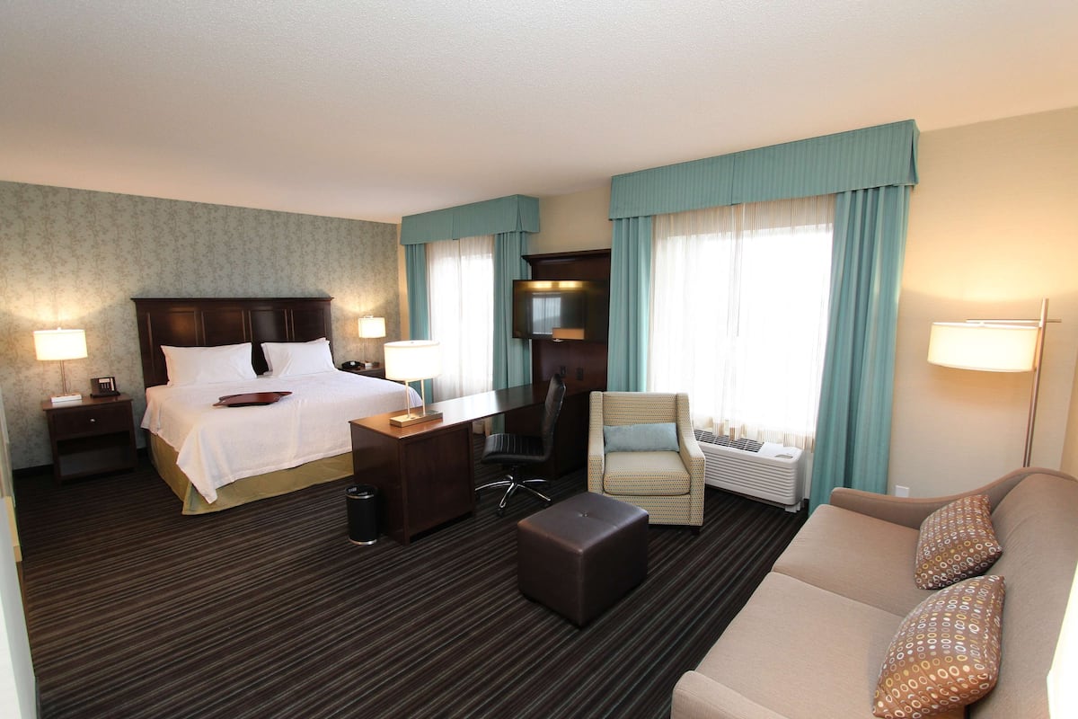 A hotel room with a bed, a desk, a chair, a sofa, and a TV.