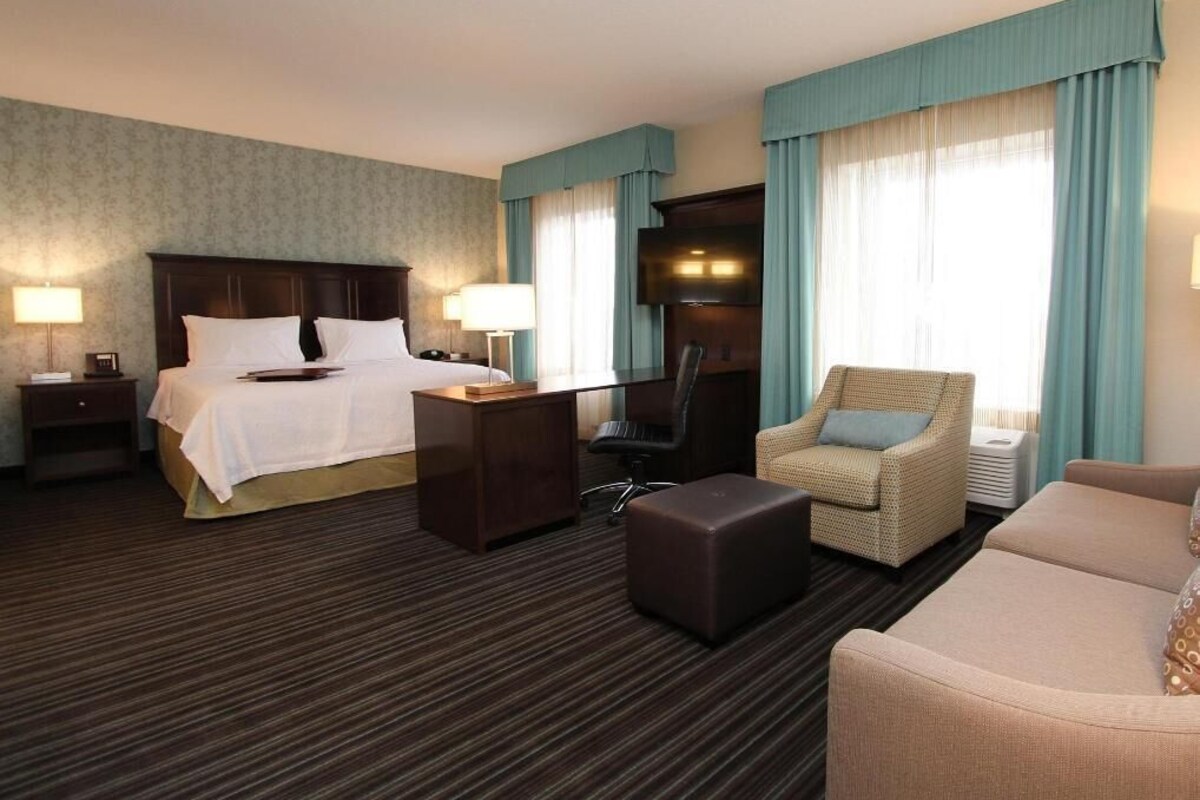 Habitación de hotel con cama, escritorio, silla, sofá y televisor.