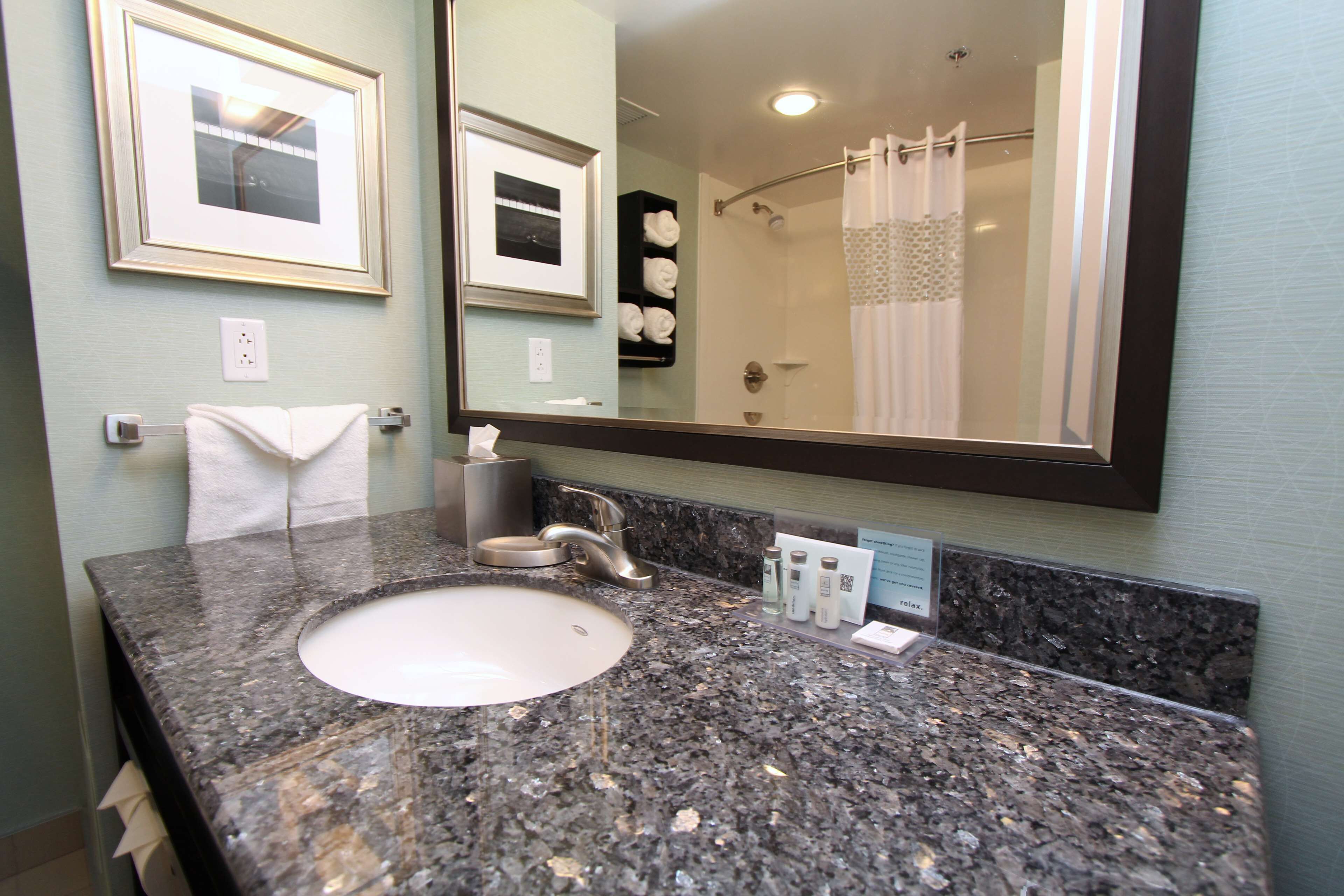 A bathroom with a granite countertop sink, a large mirror, framed pictures on the wall, and a shower curtain.