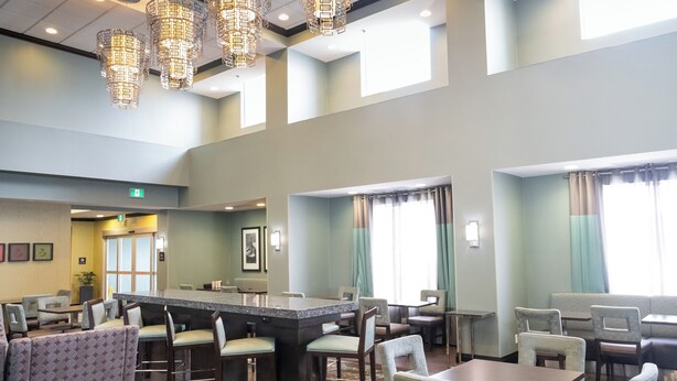 Un hall d’hôtel spacieux doté d’un bar central, de plusieurs espaces aménagés pour s’asseoir et de grandes fenêtres laissant entrer la lumière naturelle.