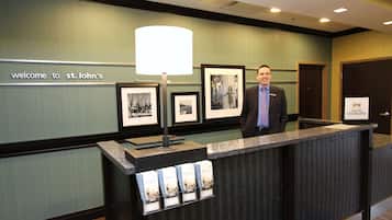 A reception desk at St. John's with framed pictures, a welcome sign, and a lamp.