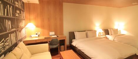 A hotel room with a large bed, a desk with a chair, a bookshelf, and a small table.