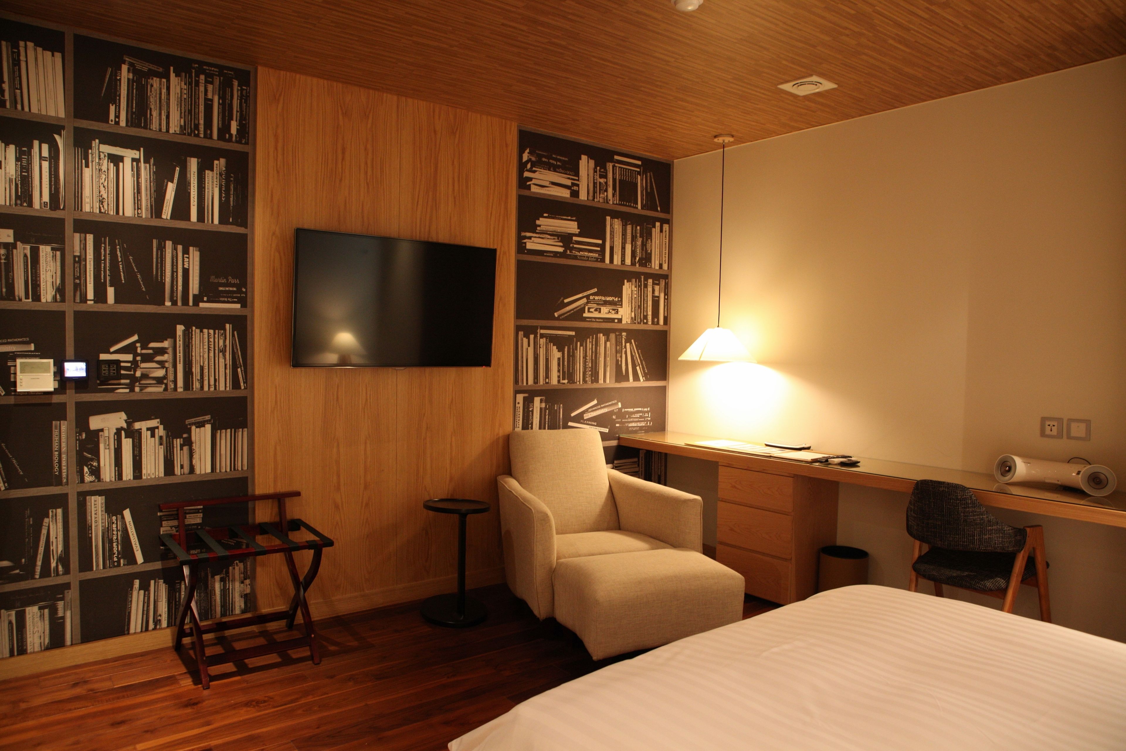 A hotel room with a large bookshelf, a desk, a chair, and a bed.
