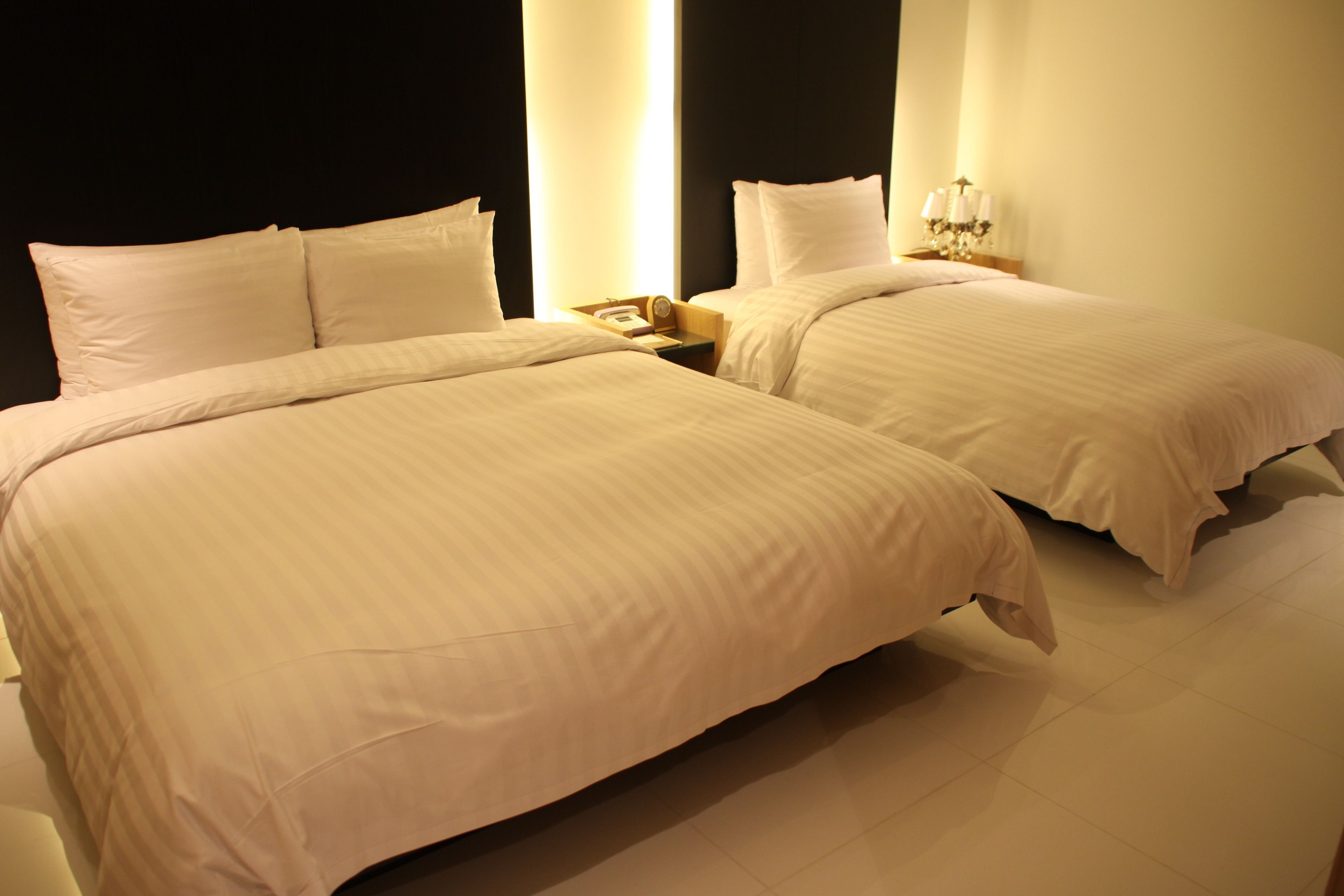 A hotel room with two beds, a nightstand with a lamp, and a large window with curtains.