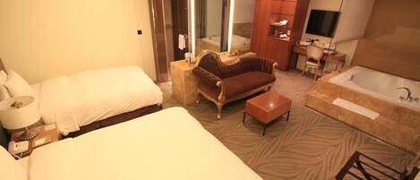 Habitación de hotel con una cama grande, un sofá, una mesita, una bañera y un espejo.