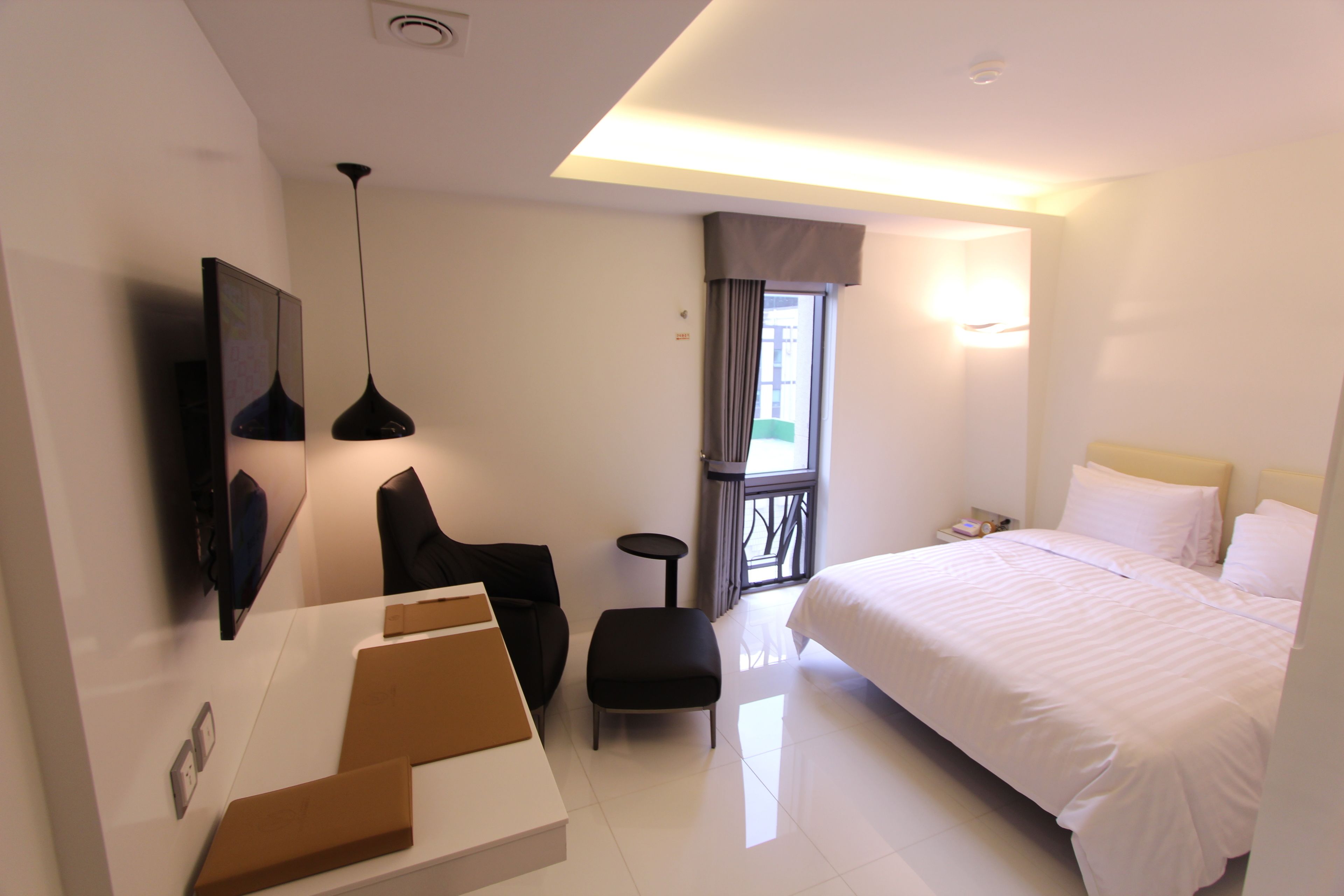 A modern hotel room with a large bed, a desk, a chair, a small table, and a TV mounted on the wall.