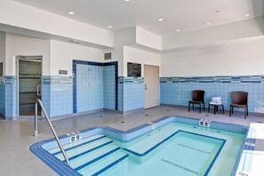 An indoor swimming pool with clear lane markings, a lifeguard chair, and a changing room area.