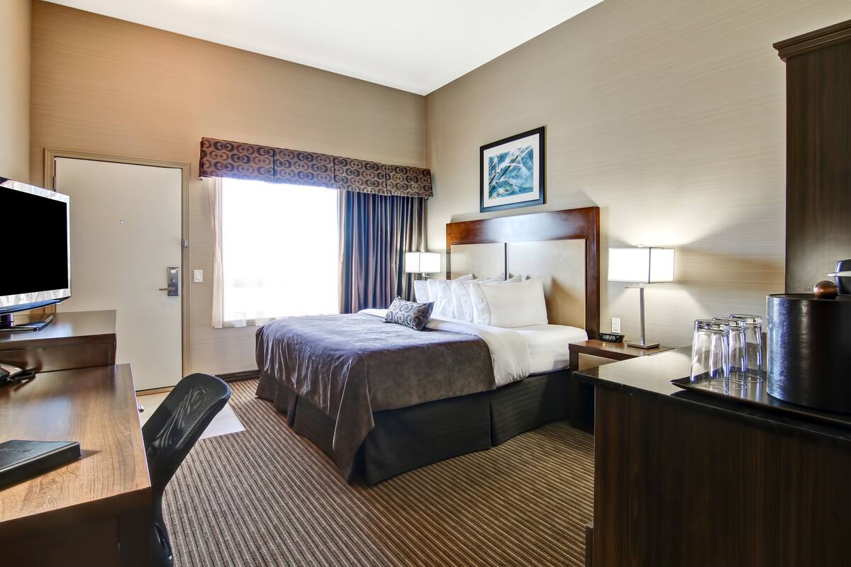 A hotel room with a bed, desk, TV, and a window with curtains.