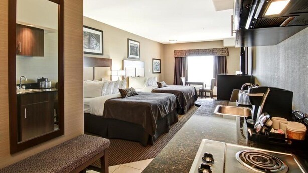 Habitación de hotel con cama, mesita de noche y escritorio con silla. Se ve una ventana con cortinas y vistas al exterior.