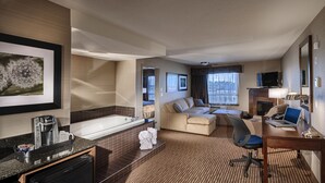Habitación de hotel con kitchenette, una cama grande, un sofá, un escritorio con una computadora portátil, un televisor y chimenea.