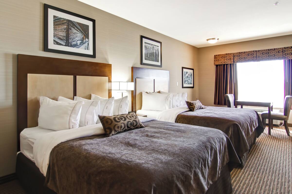 A hotel room with two beds, a desk, and a chair. There are framed pictures on the wall.