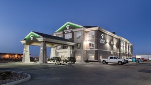 Un hotel con fachada de piedra, un acceso cubierto y varios vehículos estacionados frente a él.