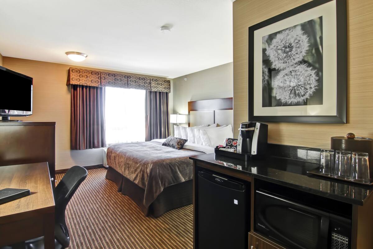 A hotel room with a bed, desk, microwave, and a framed picture on the wall.