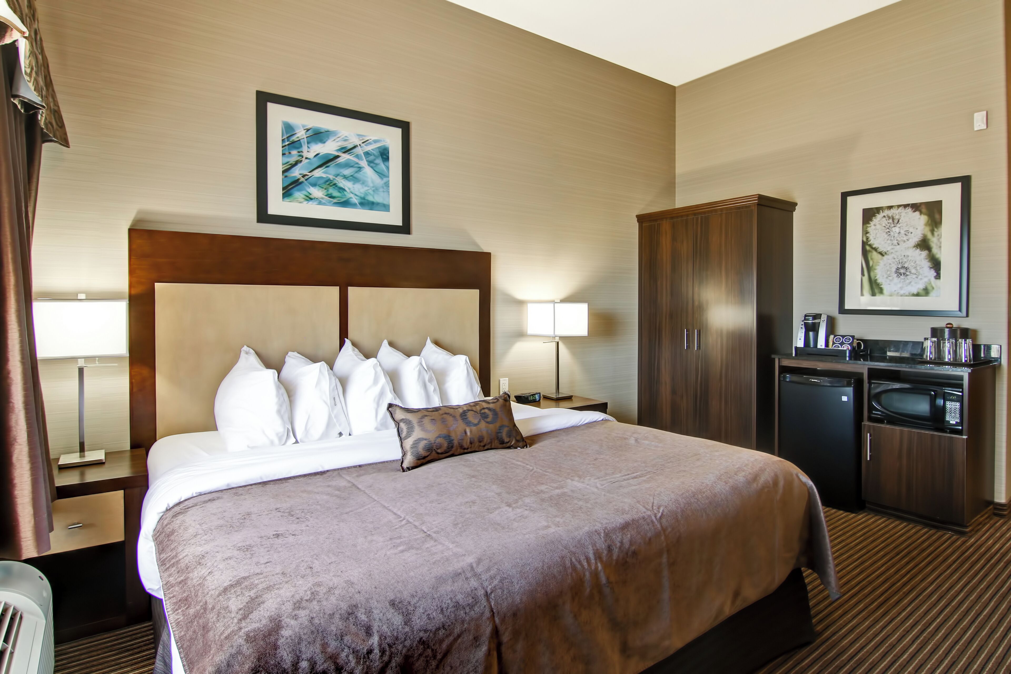 A hotel room with a large bed, a wooden headboard, a desk with a lamp, a microwave, and a cabinet.