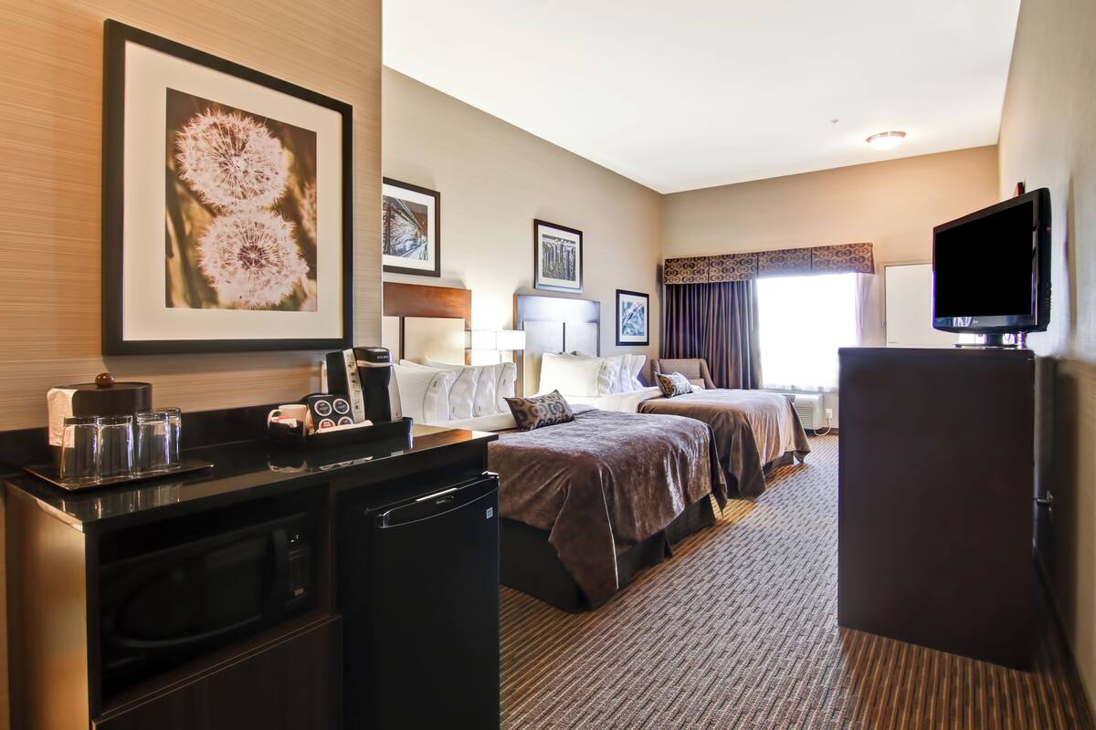 A hotel room with a kitchenette, two beds, a television, and artwork on the walls.