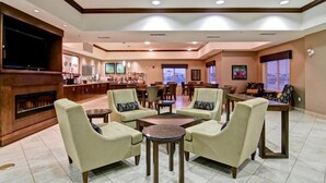 Un amplio vestíbulo de hotel con chimenea, asientos cómodos, televisor y zona de comedor.