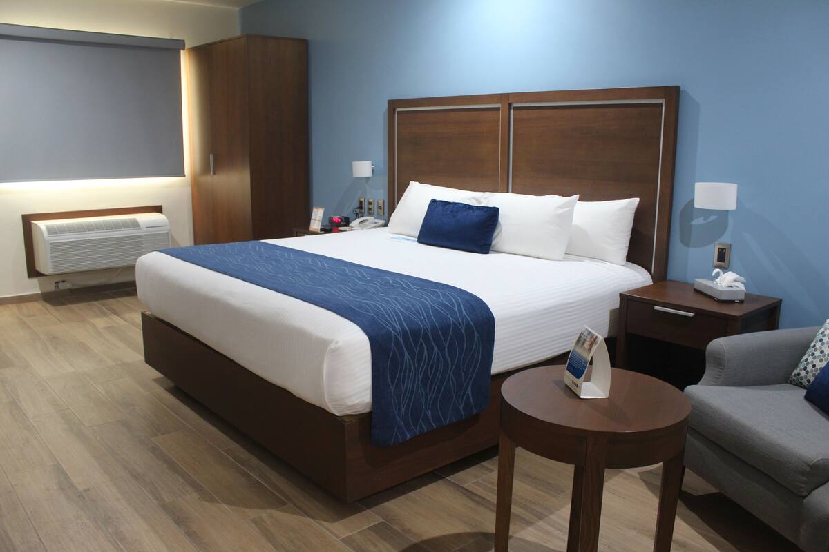 Una habitación de hotel con una cama grande, una mesita de noche, una silla y un calentador fijado a la pared.