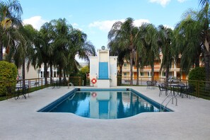 Piscina rodeada por palmeiras e assentos externos.