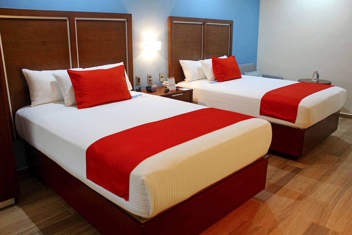 Dos camas dobles con ropa de cama roja y blanca, cabeceros de madera y una mesita de noche con teléfono y lámpara.