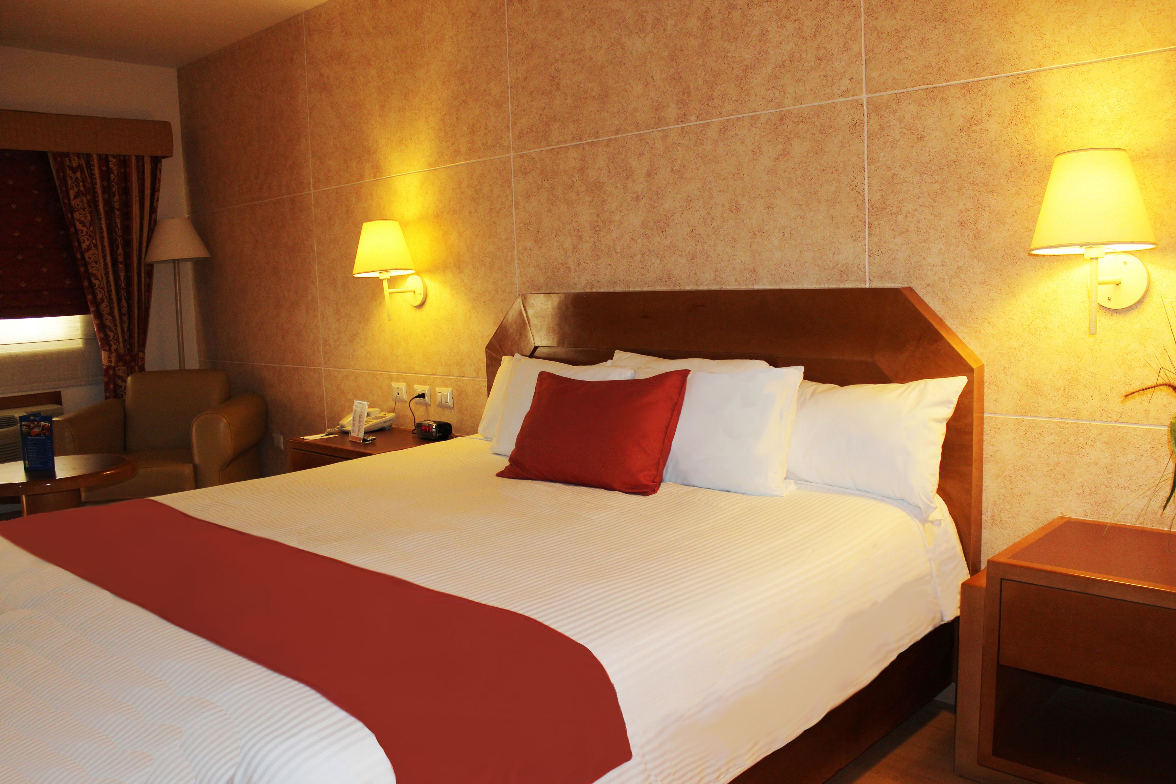 A hotel room with a large bed, two bedside lamps, a nightstand, a chair, and a window with curtains.