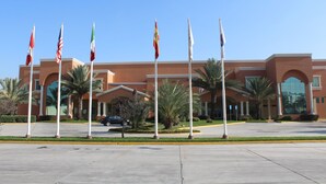 A building with multiple flags, palm trees, and a parking lot. - Comfort Inn Monterrey Norte (San Nicolas de los Garza)