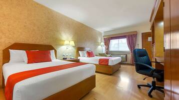 A hotel room with two beds, wooden headboards, and a desk with a chair.