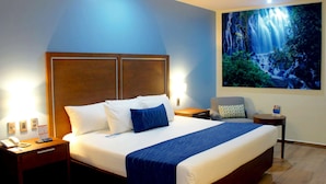 A hotel room with a large bed, a nightstand with a phone and remote, a small table with a lamp, and a painting of a waterfall on the wall. - Comfort Inn Monterrey Norte (San Nicolas de los Garza)