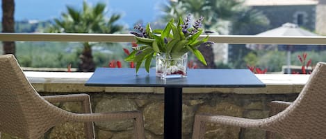 A table with a vase of flowers, two wicker chairs, and a view of the ocean.