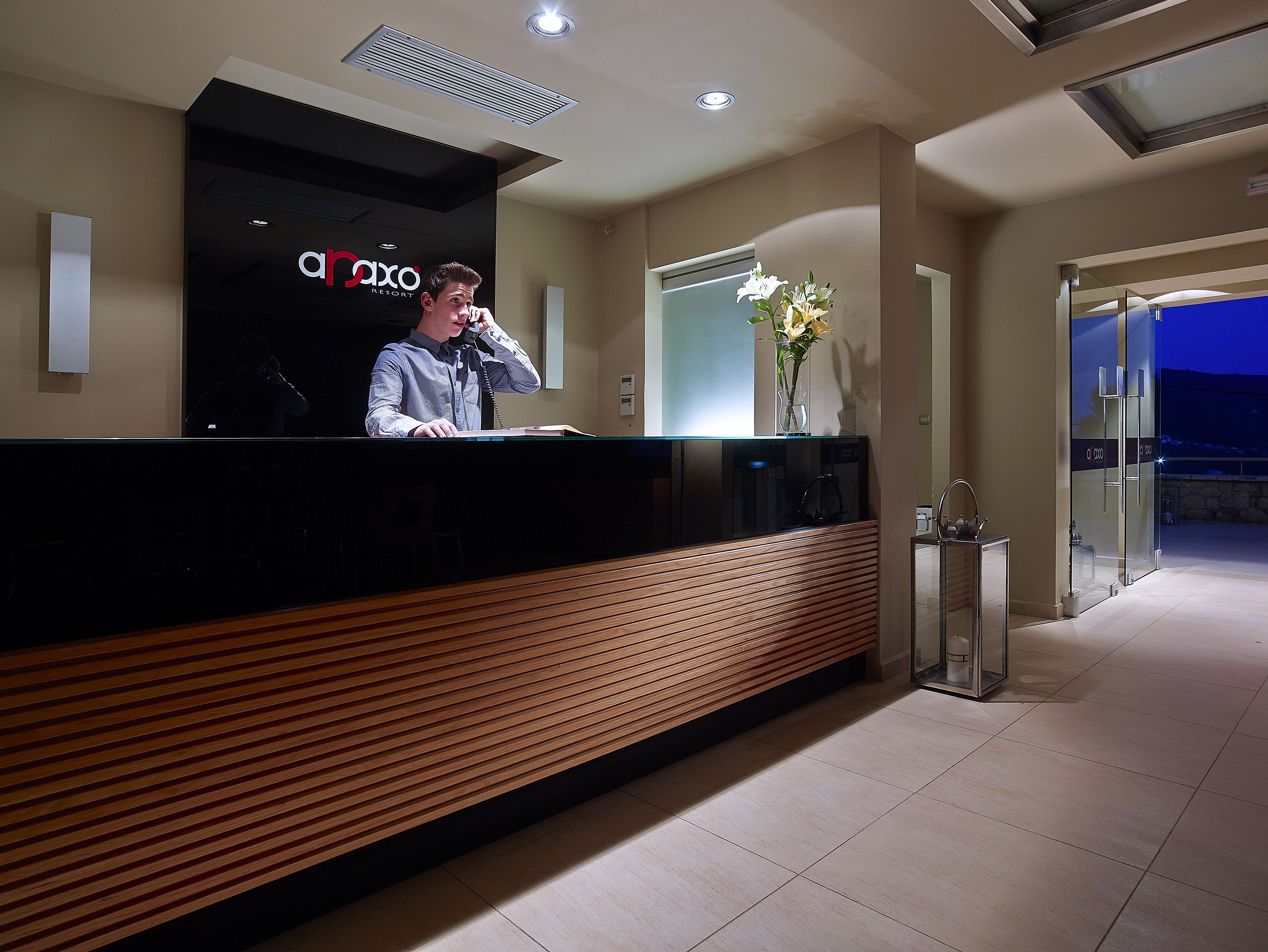 A reception desk with a modern design, a sign reading "Car Axo Resort," and a vase with flowers on the counter.