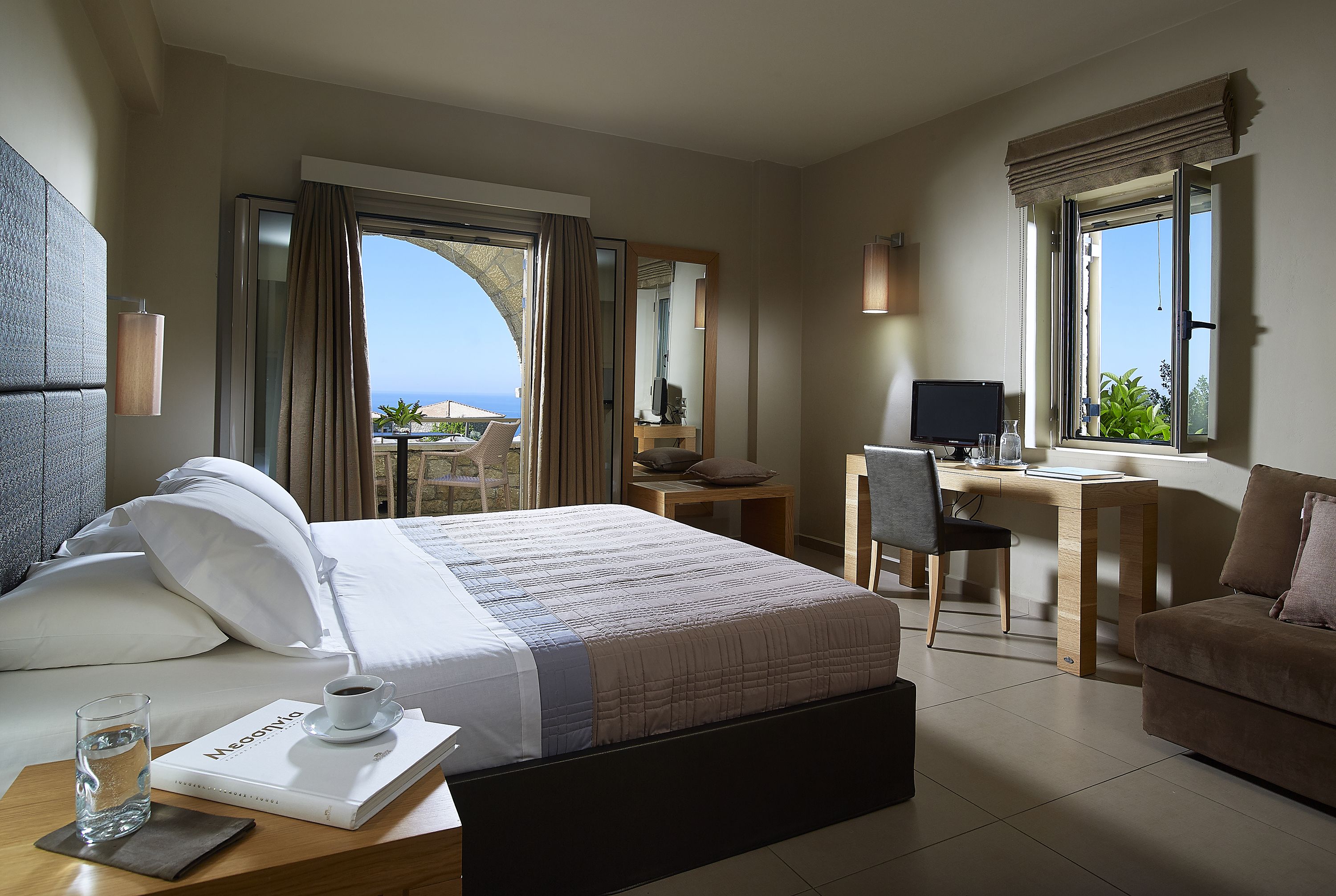 Een hotelkamer met een bed, een bureau, een stoel, een bank, een televisie en een raam met uitzicht.