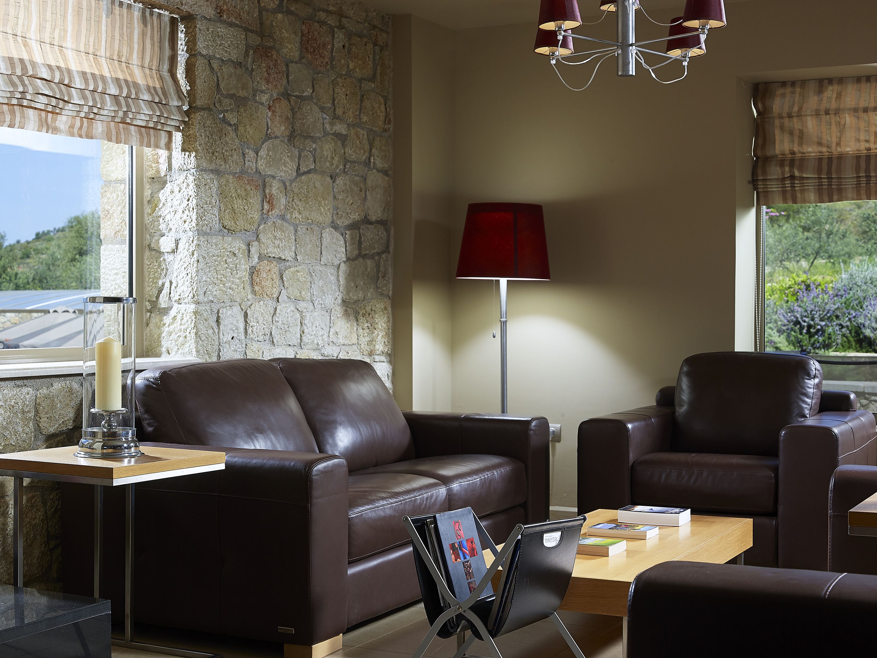 Una sala de estar moderna con pared de piedra, sofás de cuero, una mesa de centro de madera y una lámpara de pie roja.