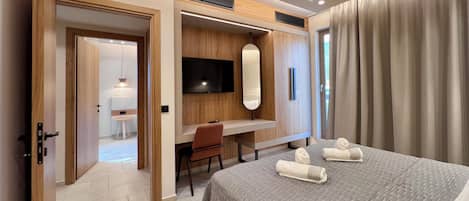 A modern hotel room with a bed, a desk, a TV, and a bathroom visible through an open door.