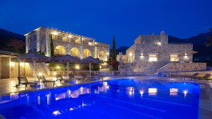 Un edificio de piedra con piscina, zona de estar al aire libre y montañas al fondo.