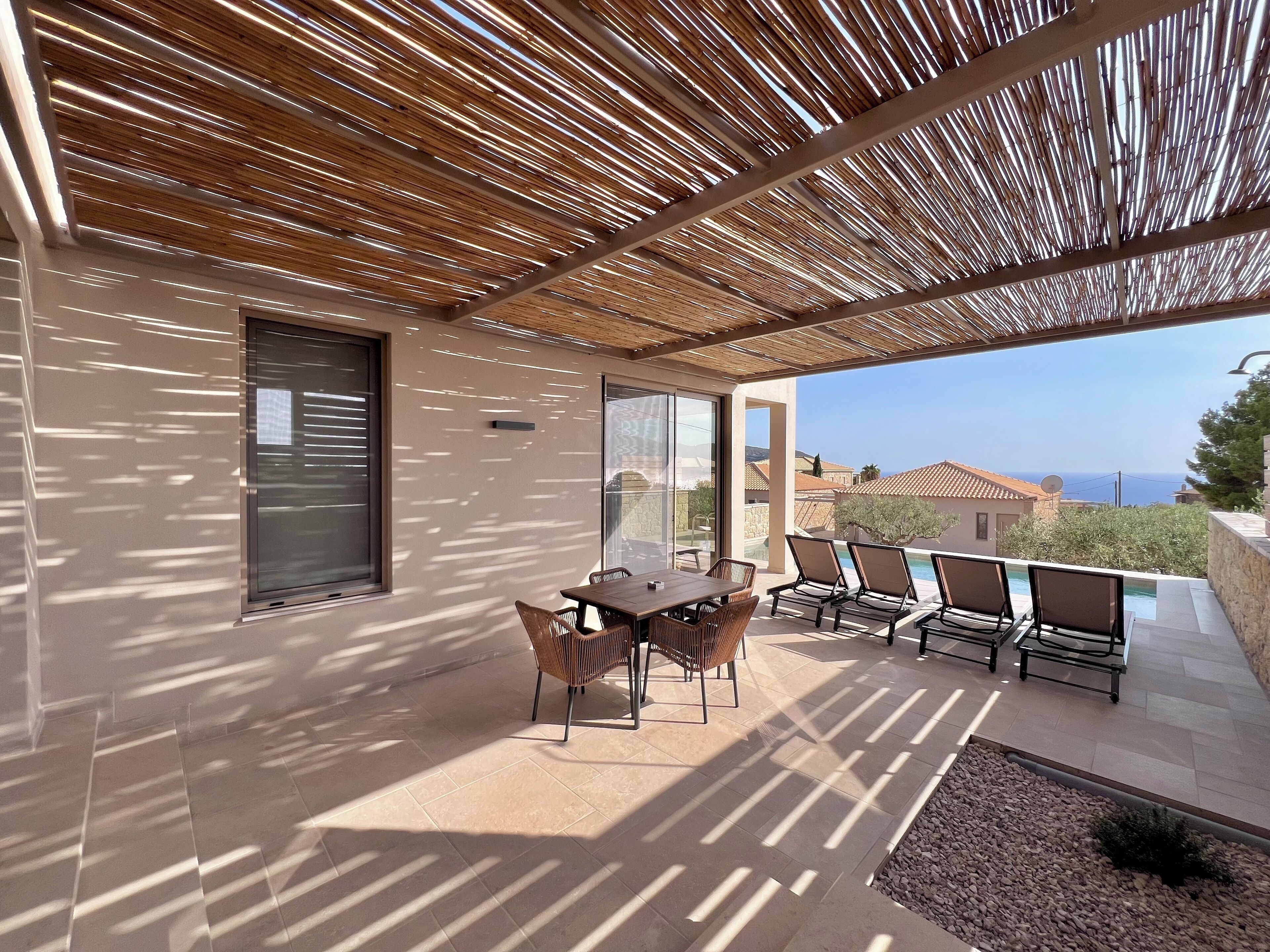 Un espacio al aire libre cubierto con una mesa y sillas, un área de descanso junto a la piscina y vistas al mar.