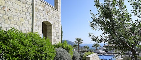A stone building with a clear view of a pool area, surrounded by greenery and a clear sky.