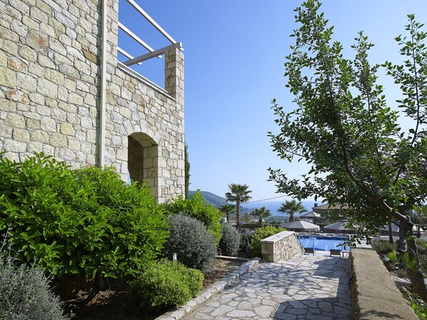A stone building with a clear view of a pool area, surrounded by greenery and a clear sky. - Anaxo Resort (West Mani)