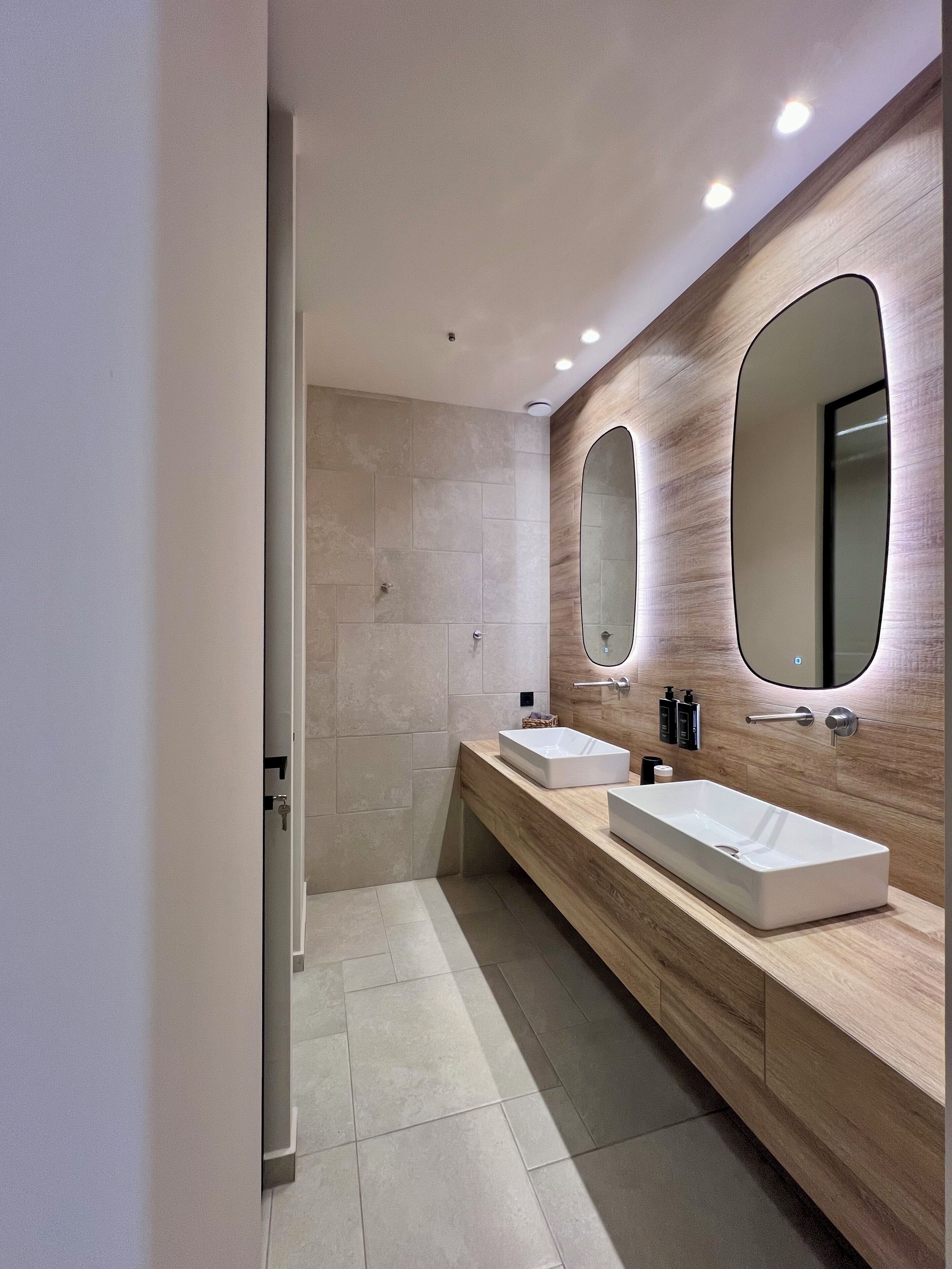 A modern bathroom with two sinks, a large mirror, and a shower area.