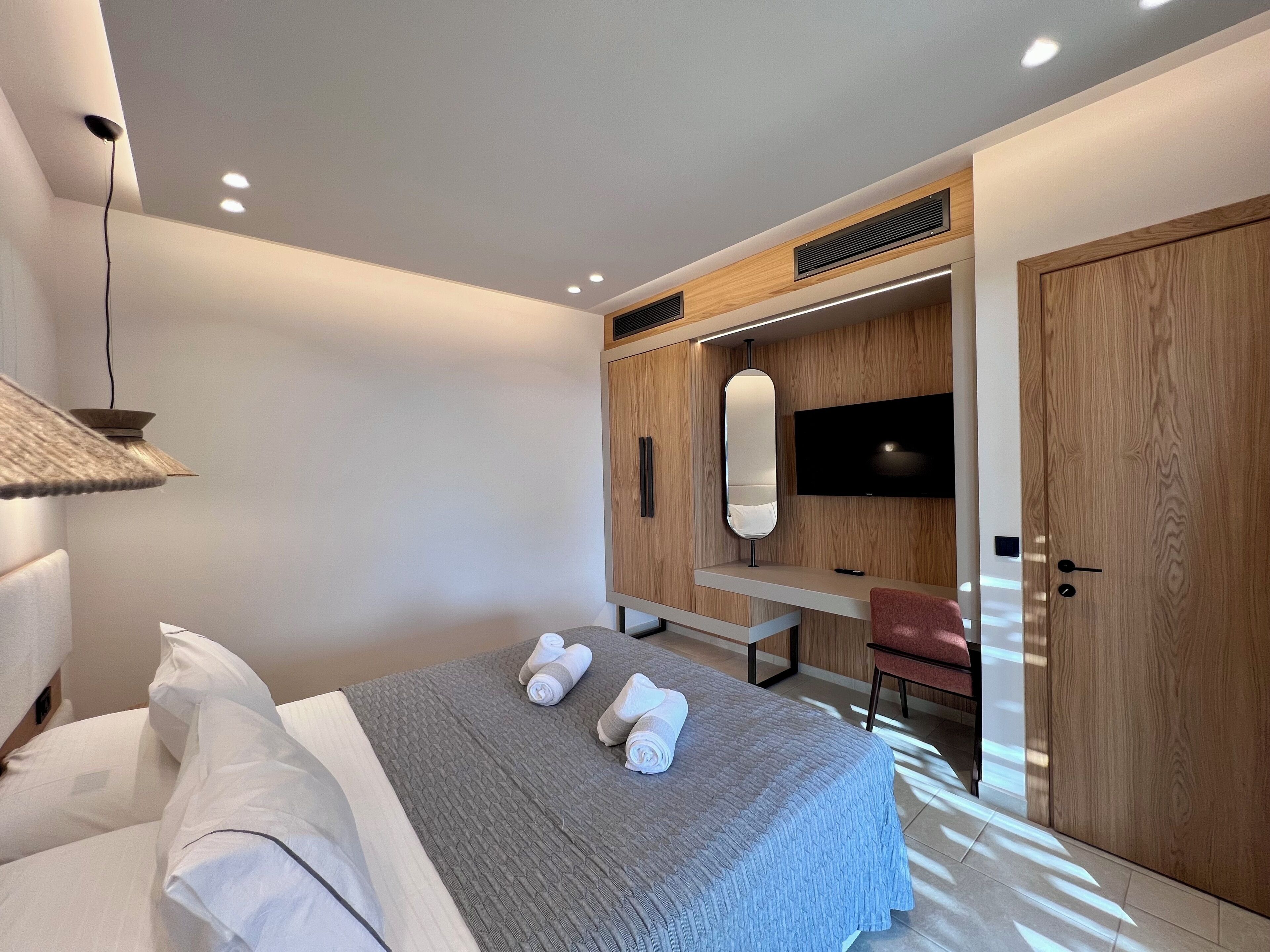 A modern bedroom with a bed, a desk, a TV, and a wardrobe.
