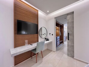 A modern hotel room with a wooden panel wall, a flat-screen TV, a round mirror, a marble countertop, and a chair.