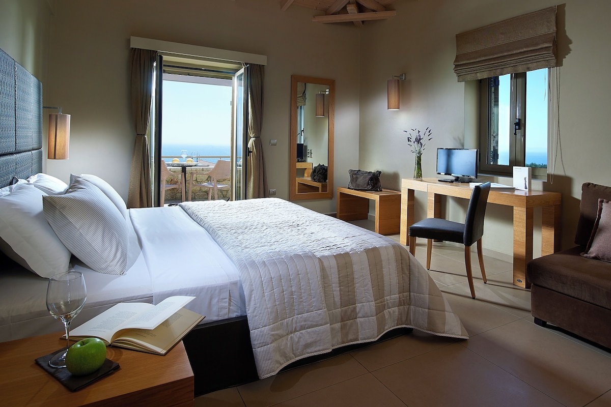 Quarto de hotel com cama, escrivaninha, cadeira, televisão e varanda com vista.
