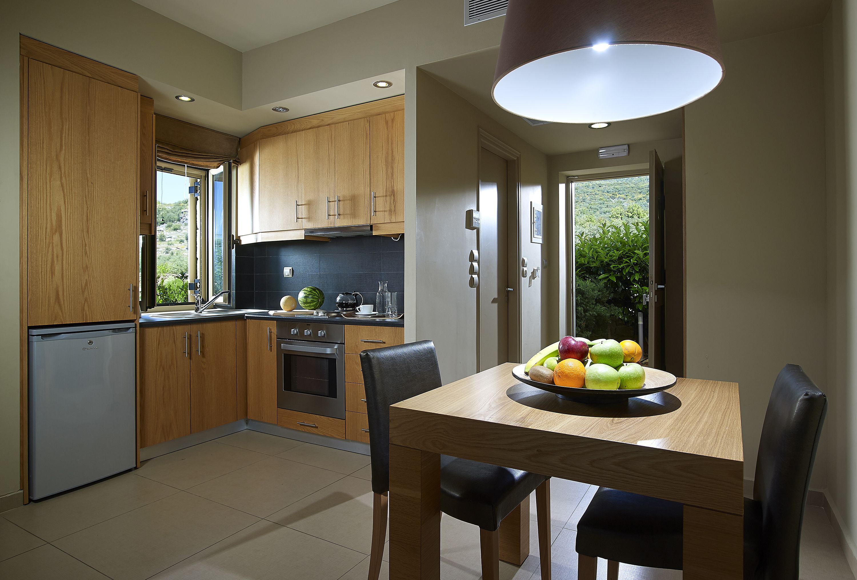 A modern kitchen with wooden cabinets, a built-in oven, and a dining area with a table and chairs.