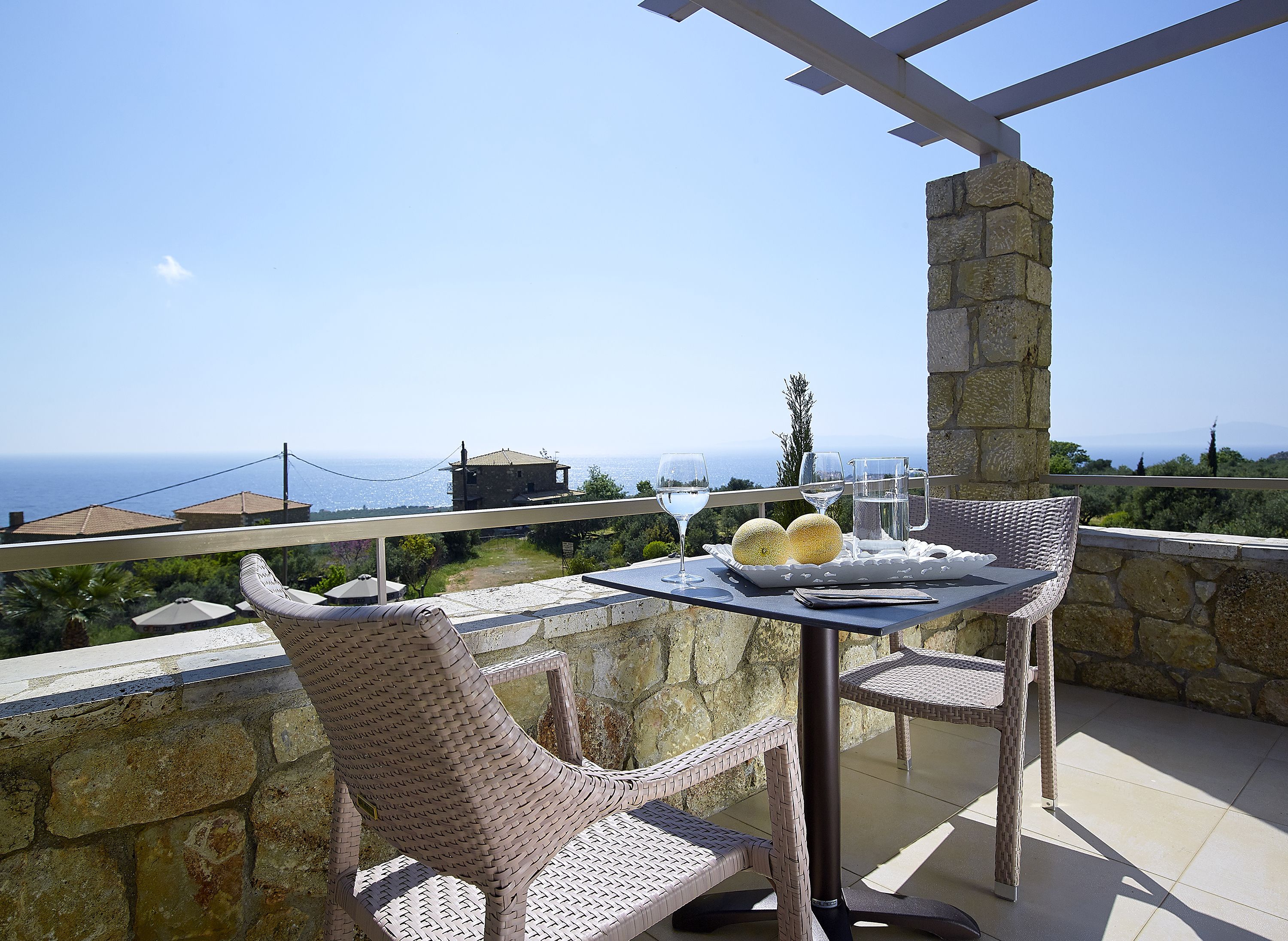 A balcony with wicker chairs, a table with a tray, and a view of the sea.