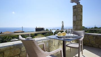 Un balcon avec des fauteuils en osier, une table avec un plateau, et une vue sur la mer.