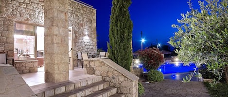 A stone building with a pool, outdoor seating, and a staircase leading to the entrance.