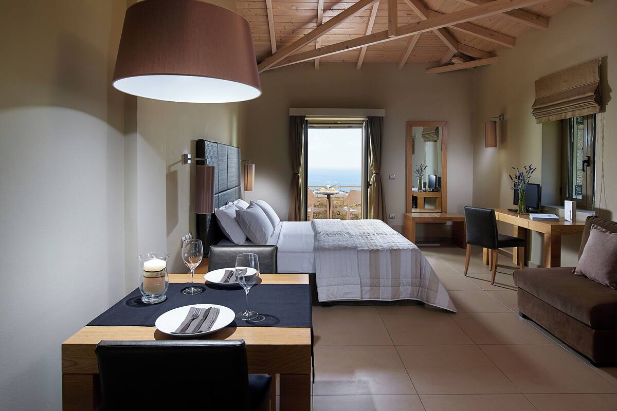 Ein Hotelzimmer mit Bett, Schreibtisch, Esstisch mit Stühlen und Meerblick.