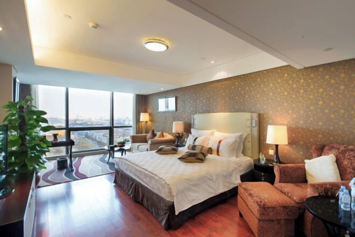 A hotel room with a large bed, a sitting area with a sofa and armchairs, a small table, and a view of the city.