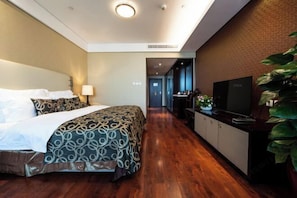A hotel room with a bed, a TV, a desk, and a plant. - Hua Bin International Hotel (Beijing)
