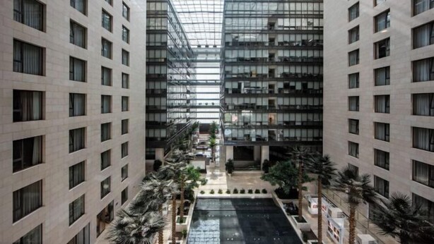 Een modern gebouw met meerdere verdiepingen, grote ramen en een centrale binnenplaats met palmbomen.