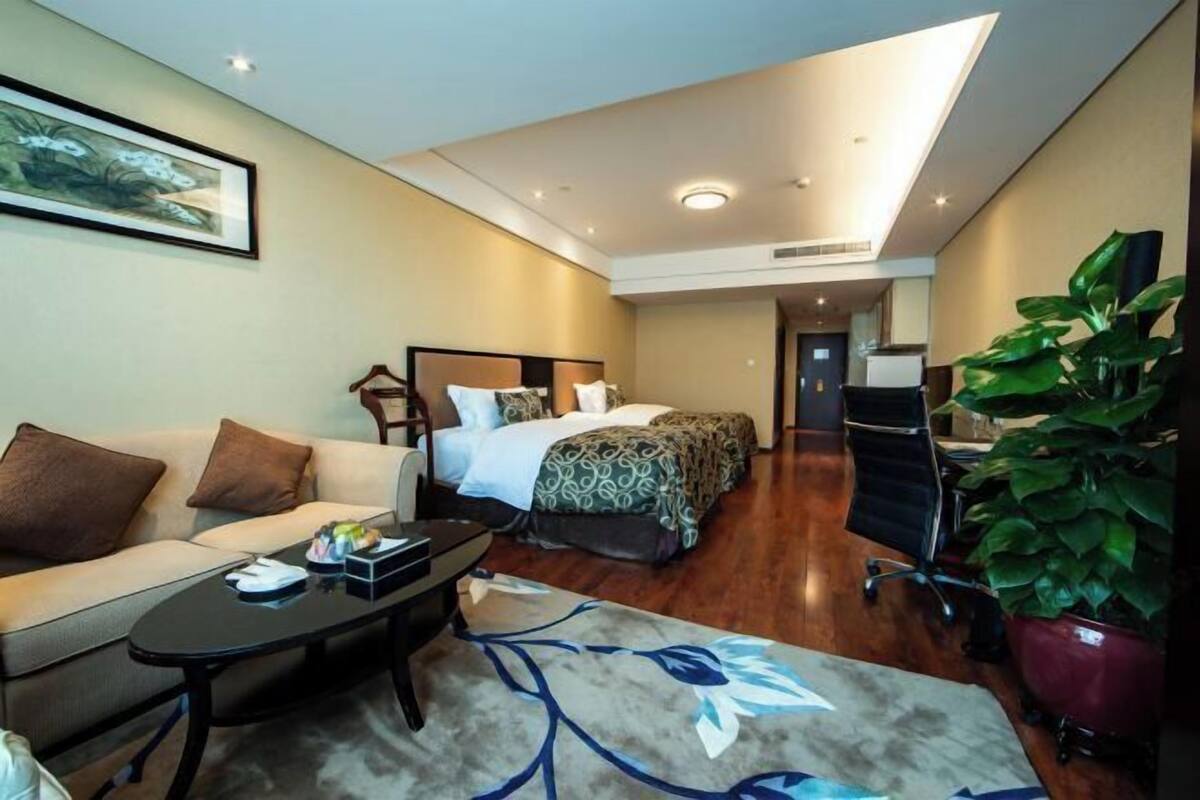 Ein Hotelzimmer mit Bett, einer Couch, einem Schreibtisch und einer Zimmerpflanze.