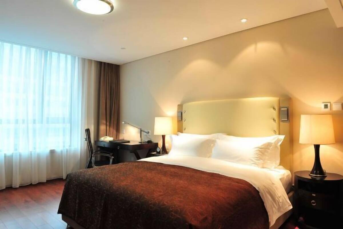 Ein Hotelzimmer mit einem großen Bett, zwei Nachttischlampen, einem Schreibtisch mit Stuhl und einem fenster mit Vorhängen.
